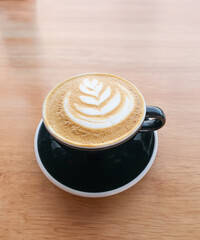 Caffè Latte in black cup and saucer on wooden table with frothy art