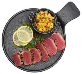 Sliced Organic grilled Tuna fillet covered with sesame seeds and mango salsa on black ceramic serving board