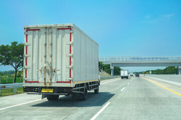 A white cargo delivery truck is driving on the highway with empty space