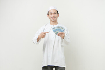 muslim man holding money rupiah banknotes and give pointing finger gesture. People religious Islam lifestyle concept. celebration Ramadan and ied Mubarak. on isolated background.