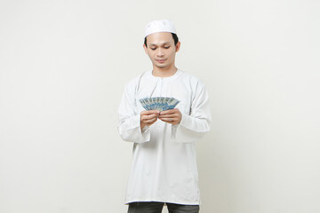 happy muslim man holding money rupiah banknotes. People religious Islam lifestyle concept. celebration Ramadan and ied Mubarak. on isolated background.