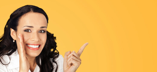 Happy excited smiling businesswoman keep hand near face, showing indicating copy space. Amazed business woman covering mouth with palm, pointing away side by index finger, isolated yellow. Wide banner