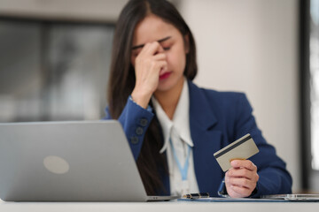 stressed young businesswoman with a credit card in hand, looking worried in front of her laptop.