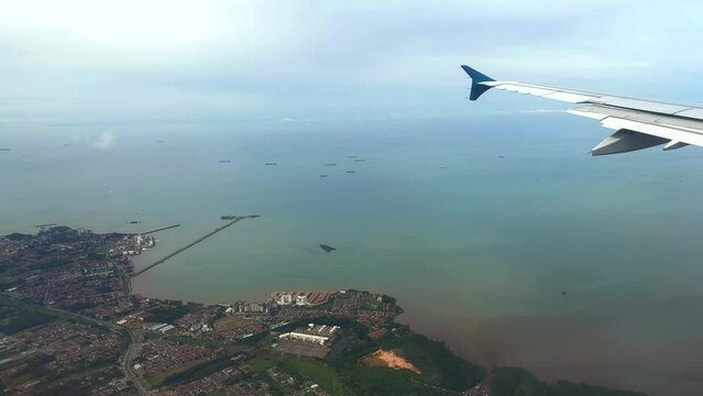 Aerial view of ships waiting off the coast of Malaysia through airliner window. View of cargo ships waiting off coastline through plane window.