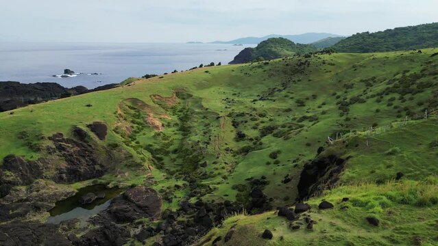 Stunning aerial rising view of lush green hills and rocks with island paradise in background. Catanduanes, Philippines