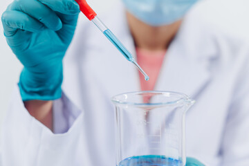 A scientist examines samples with a microscope in a laboratory with test tubes filled with colorful...