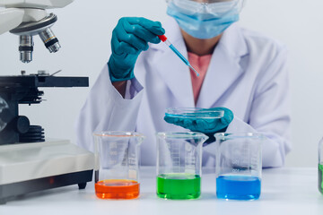 A scientist examines samples with a microscope in a laboratory with test tubes filled with colorful...