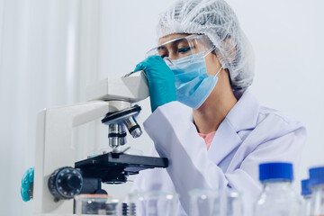 A scientist examines samples with a microscope in a laboratory with test tubes filled with colorful...