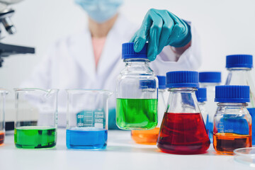 A scientist examines samples with a microscope in a laboratory with test tubes filled with colorful...
