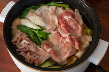 Pot of shabu with meat sliced and vegetables in soup. Delicious shabu at home on wooden table background.