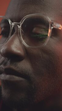 Vertical closeup of green programming code reflecting in eyeglasses on Black male programmer