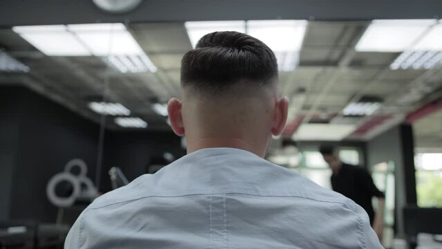 A young man in a barbershop after a haircut. Modern and stylish haircut. Back view. Slow motion, hairdryer
