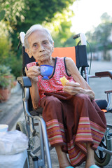 asian old woman sitting on whell chair and drinking warm beverage