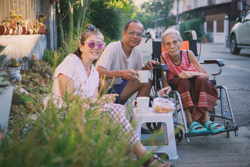 asian family with grand mama sitting on wheel chair enjoy morning coffee at home village