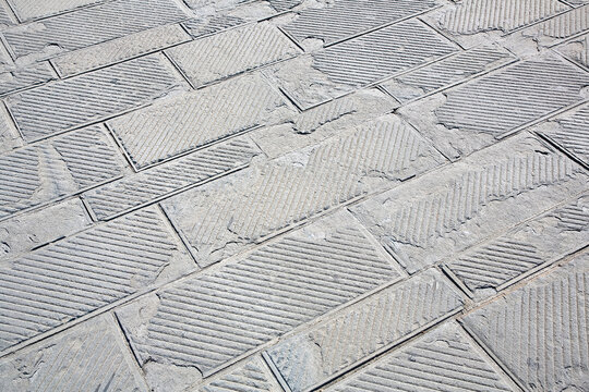 Old and damaged italian paving made with chiseled grey sandstone blocks in a pedestrian zone - The surface part is being damaged due to the freeze and thaw cycles that break the stone