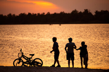 Silhouettes of children and bicycles against the background of the sunset sky on the embankment by the river. Ukraine. Hola Prystan, Kherson region. Today it is occupied territory.  © Ann Stryzhekin