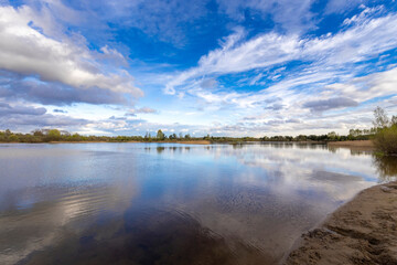 Fototapeta na wymiar Forest on the horizon. The spring sky is reflected in the water. dramatic clouds