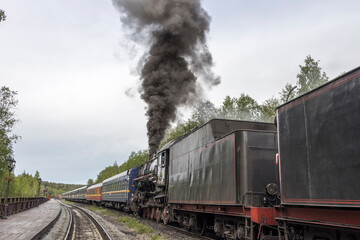 Steam locomotive at the station. An antique locomotive with carriages, powered by steam. black smoke from the locomotive chimney