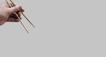 Asian chopsticks held in human hands on monochrome dark pink background. Without food. No identifiable person. Wide free space for layout of text and other content	
