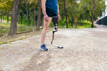 Side view of an unrecognizable man with a sports prosthetic leg, ready for a run in a leaf-strewn park path.