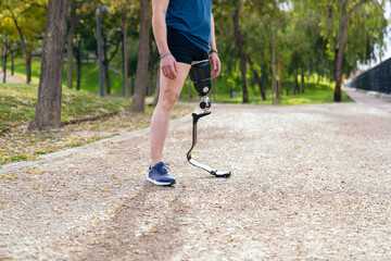 Side view of an unrecognizable man with a sports prosthetic leg, ready for a run in a leaf-strewn...