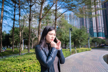 Beautiful woman with long hair in black leather jacket using mobile phone on the park