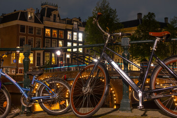Fototapeta na wymiar Adult and Children's Bikes on the Canal Embankment in Amsterdam at Night