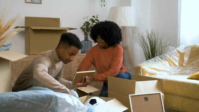 Young black couple packing in a moving cardboard boxes to settle in a new home. New residence relocation.