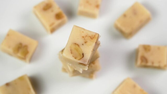 Classic Spanish sliced Turron with almonds stacked in tower shape on a white ceramic dish. Hand taking one sweet piece close up