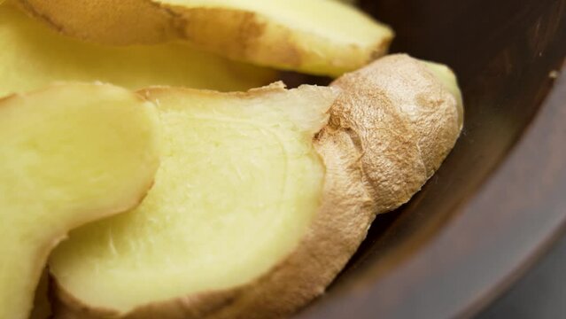 Sliced ginger roots in rustic wooden bowl. Slices of fresh zingiber rhizome. Rotation. Studio shot