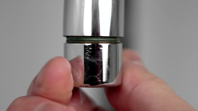Hand of a repairman installs the aerator filter of a chrome kitchen faucet. Home equipment maintenance and plumbing concept. Macro shot