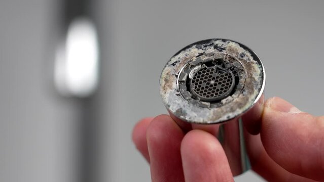 A plumber is holding a chrome faucet aerator with lime scale in kitchen room