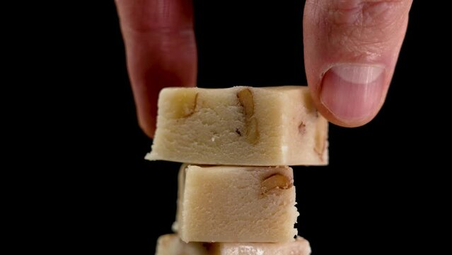 Classic Spanish sliced Turron with almond nuts stacked in tower shape. Hand taking one delicious piece close up. Black backdrop