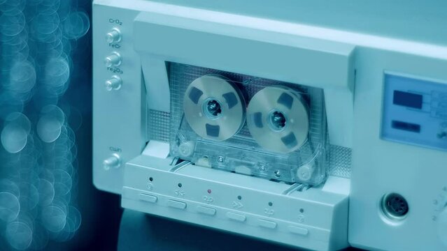 A cassette with gold reels plays music in a Hi-Fi recorder from 80s of silver  color. Closeup. Shot in motion
