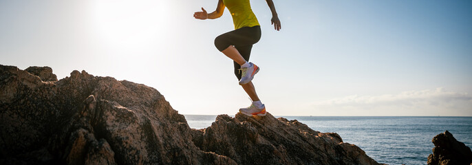 Woman runner legs running on sunrise seaside rocks
