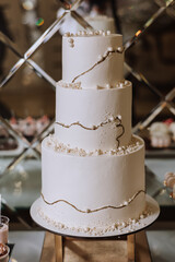 A large luxurious multi-tiered wedding cake is decorated with white pearls in the banquet hall. Wedding dessert under the evening light. Wedding decor.