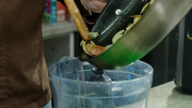 Hands of chef transferring roasted meat with onions and garlic to blender. Steam coming from hot ingredients symbolizes unique aroma