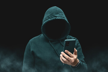 Mysterious faceless hooded anonymous hacker holding smartphone, silhouette of cybercriminal,...