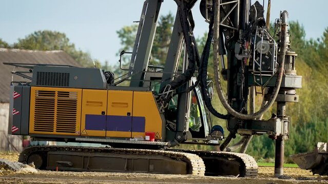 Drilling water wells. Machine lowers drill down. Slow motion. Closeup. Digs holes in ground with drilling rig. Modern rotary drill rig bore water well among green trees