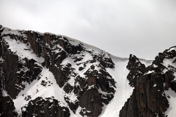 Rocks with snow cornice in gray day
