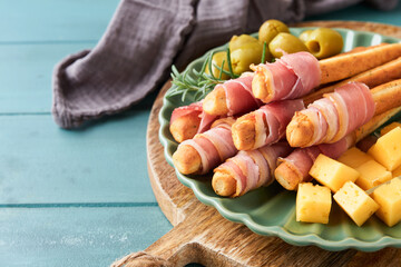 Slices of prosciutto or jamon. Delicious grissini sticks with prosciutto, cheese, rosemary, olives on green plate on dark background. Appetizers table with italian antipasto snacks Top view copy space