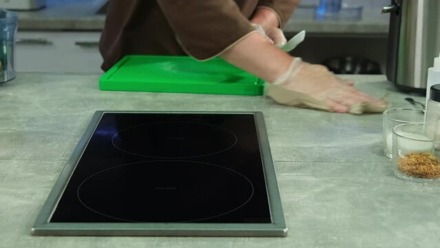 Male culinarian in gloves cleans surface of kitchen table using rag. Cook accuracy makes cooking scenes more aesthetically pleasing