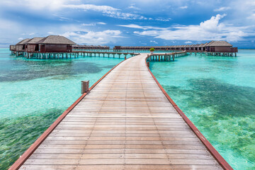 Scenic view of water villas in Maldives with turquoise pristine water and dramatic sky
