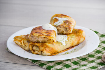 Thin fried pancakes with meat filling in a plate with sour cream and spices.