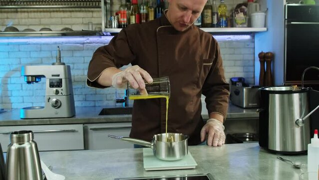Skilled chef positions saucepan on scale accurately measuring necessary amount of juice for recipe. Man pours juice into saucepan