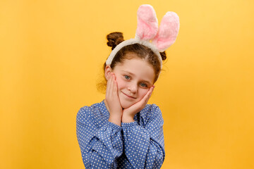 Portrait of attractive cute sweet preteen girl child wearing pink bunny ears, happy looking at camera, posing isolated over plain yellow color background wall in studio. Easter holiday concept