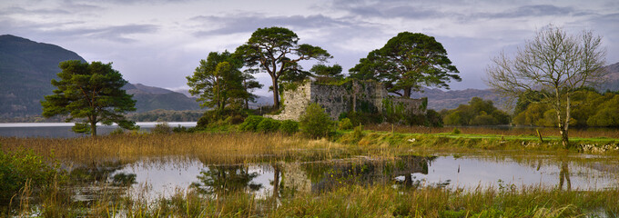 McCarthy’s Castle, Killarney, County Kerry - Republic of Ireland. Calm lake, trees, cloudy sky and mountains in the background. Beautiful Irish national park panoramic view. 