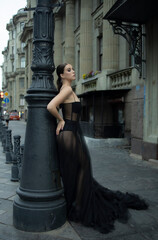 A 30-year-old girl in a black transparent revealing dress on a city street. Style and elegance, femme fatale, photo shoot, advertising, girl 
