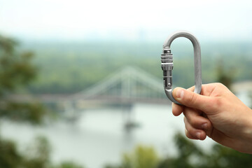 Man holding metal carabiner outdoors, closeup. Space for text