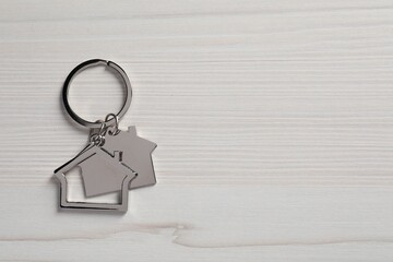 Metal keychain in shape of houses on white wooden table, top view. Space for text